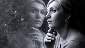 A black and white photo capturing a woman in deep self-realization as she gazes pensively out of a window.
