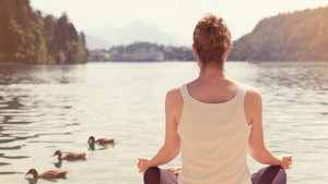 A woman is embarking on an inner quest as she meditates in front of a lake with ducks.