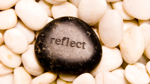 A stone with the word reflect on it, situated along a path of white pebbles, symbolizes self-realization during one's journey.