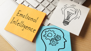 The word emotional intelligence, representing a journey towards heart-centered living, is written on a piece of paper next to a laptop, serving as a reminder of valuable lessons.