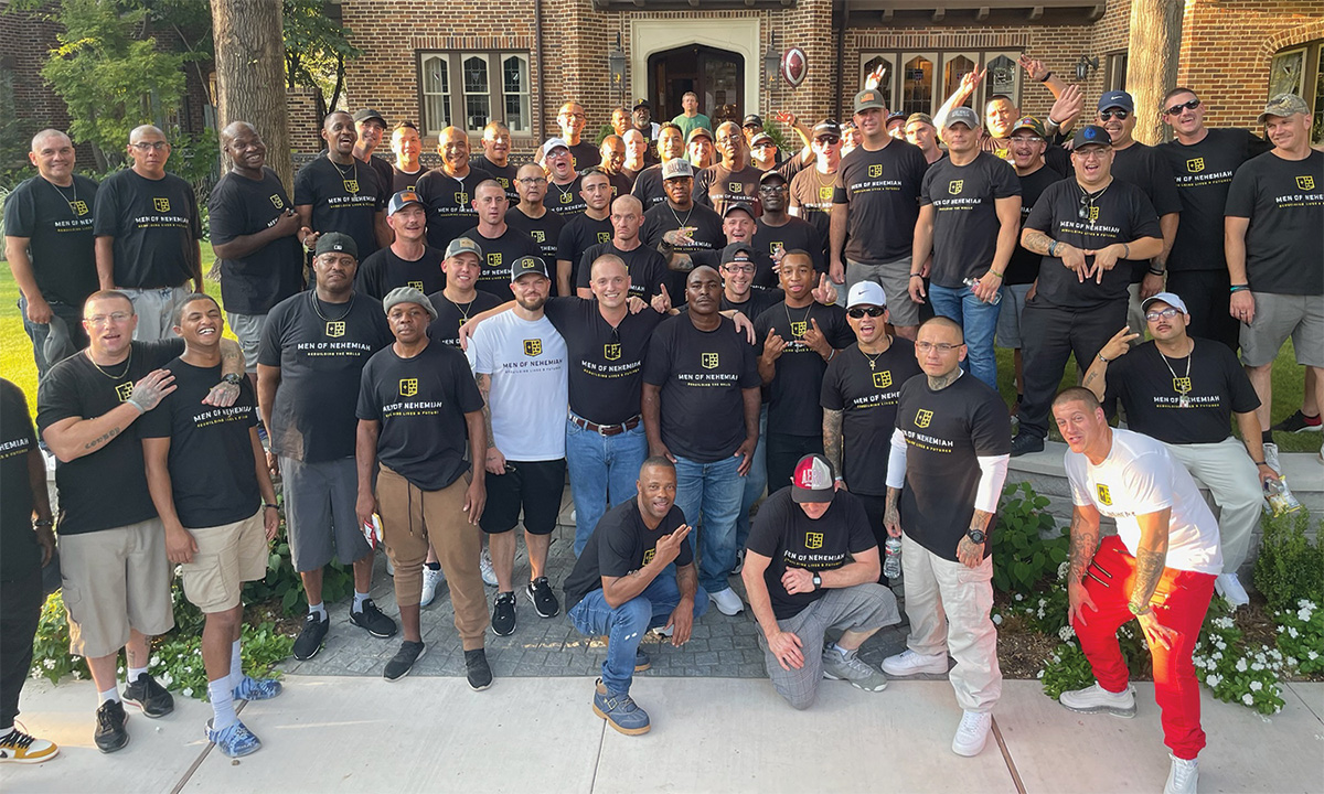 Large group of men wearing matching shirts standing together outside in front of a brick building.