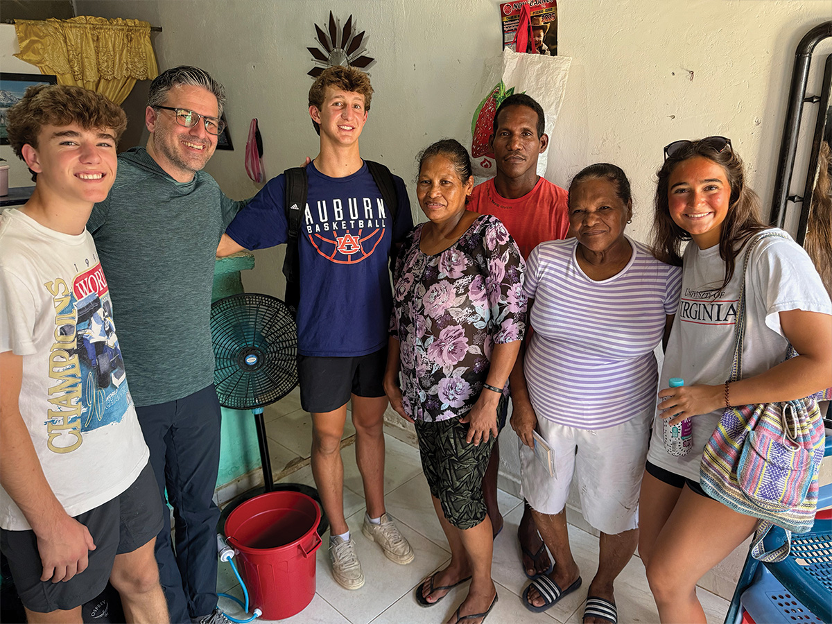 Small group of mission trip volunteers standing with a local family inside a home during a service project visit.